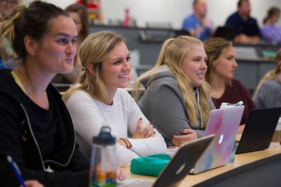 四名波胆网站女学生在演讲厅微笑的照片, 他们的笔记本电脑在他们面前打开