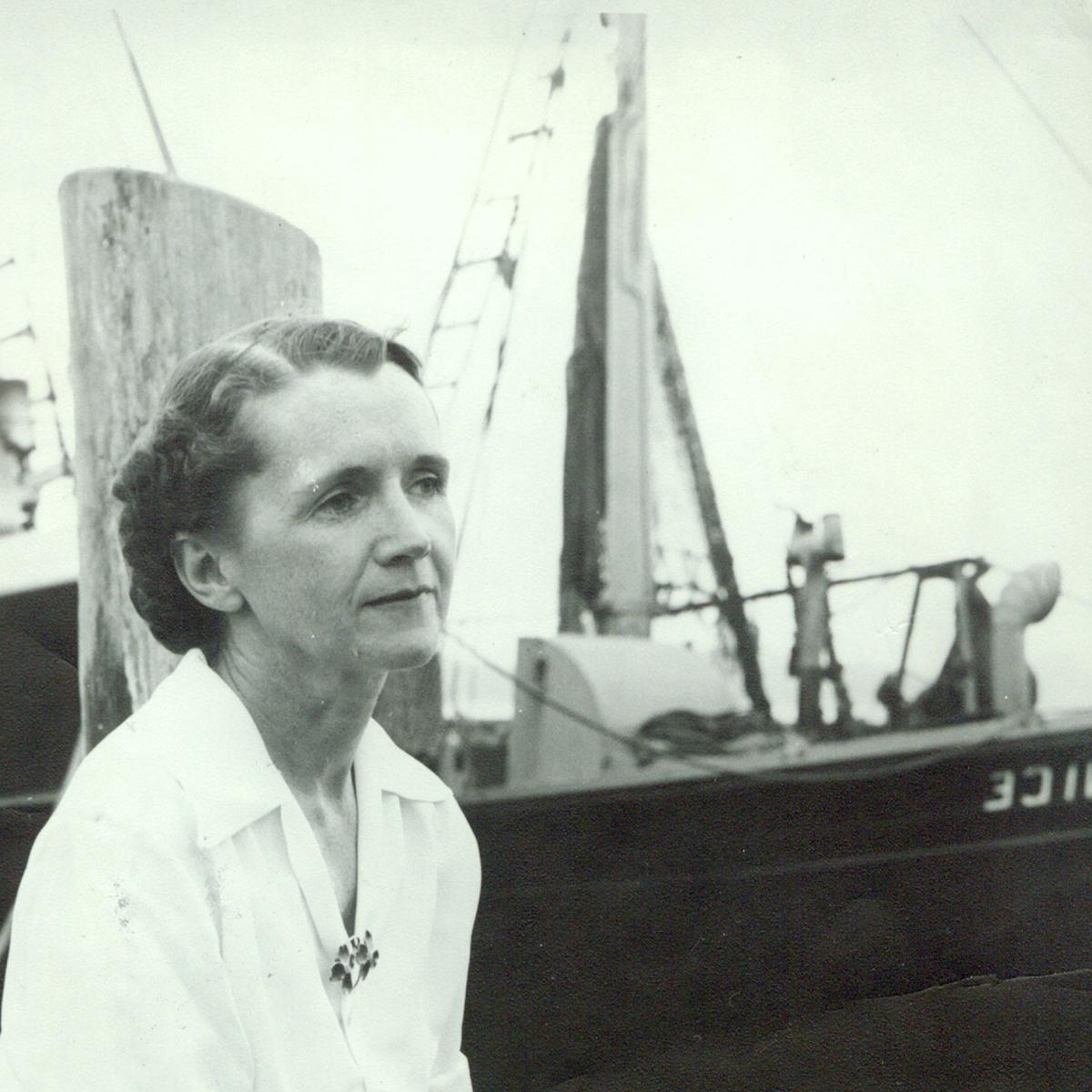 雷切尔·卡森坐在码头上的黑白照片, 她手里拿着笔和纸，背景是一艘船